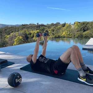 Homme réalisant un exercice d'abdos avec haltères en extérieur près d’une piscine, coaching sportif à domicile à Mandelieu
